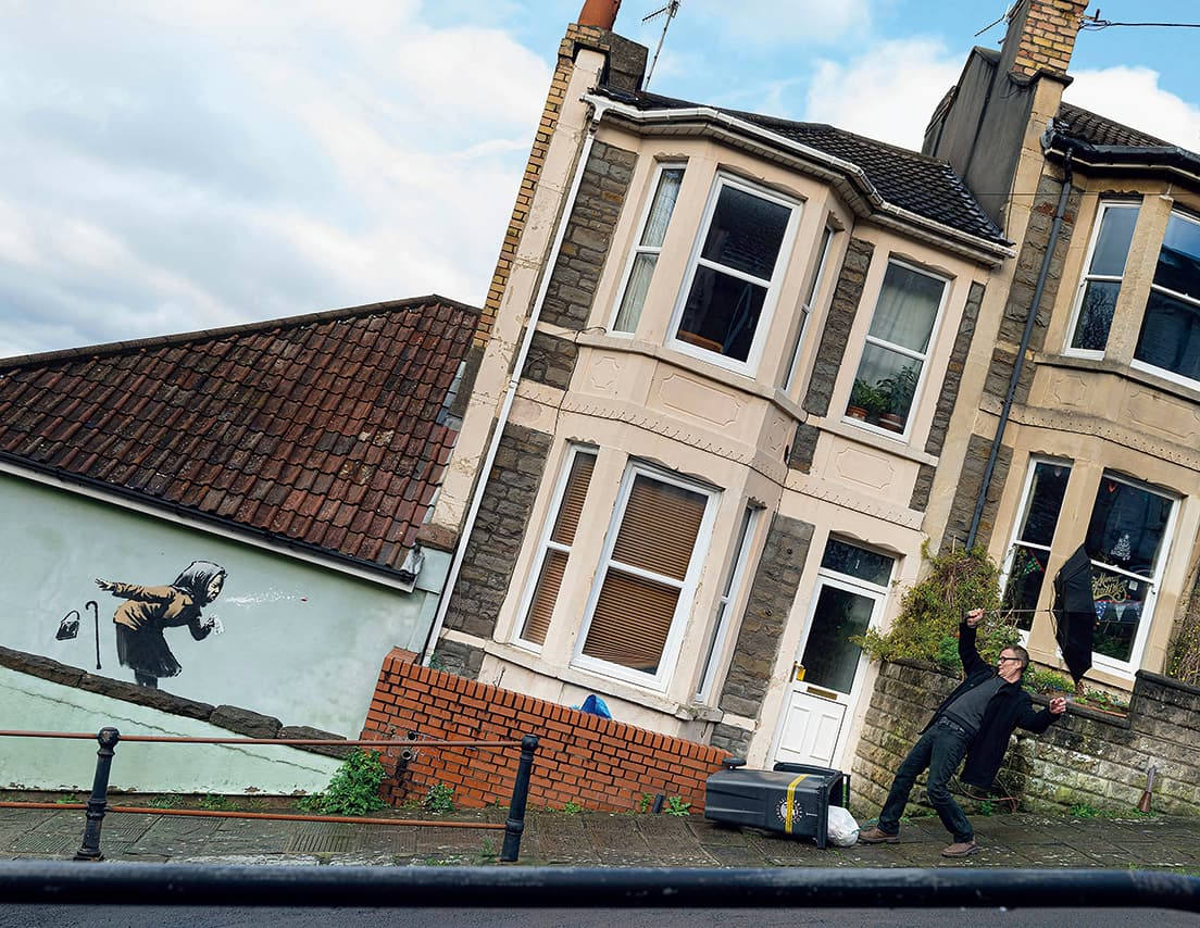 Aachoo!!（2020）Bristol, UK
2020年12月11日発表の《ハックション!!》。描かれた民家は、イースター祭に卵転がし競争が行われることで有名な急坂に面する。傾斜を水平にして写真を撮ると、くしゃみの衝撃で家や町全体が吹き飛ばされそうに見えるトリックアートになっている。おばあさんの上品な装いからは、同年11月までマスク未着用で批判されたエリザべス女王の姿も見え隠れ。courtesy of www.banksy.co.uk