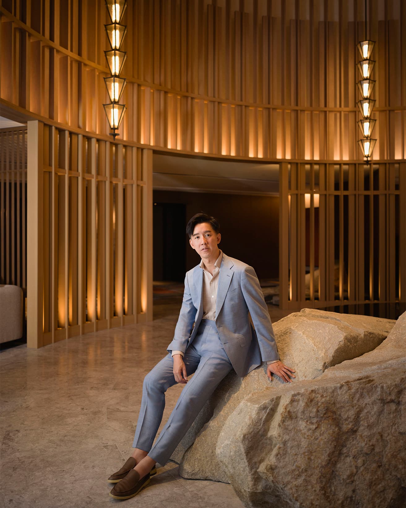チェックインロビーに設置された石のオブジェに腰掛けるアンドレ・フー。彼の考える日本的なデザインが随所に息づく。