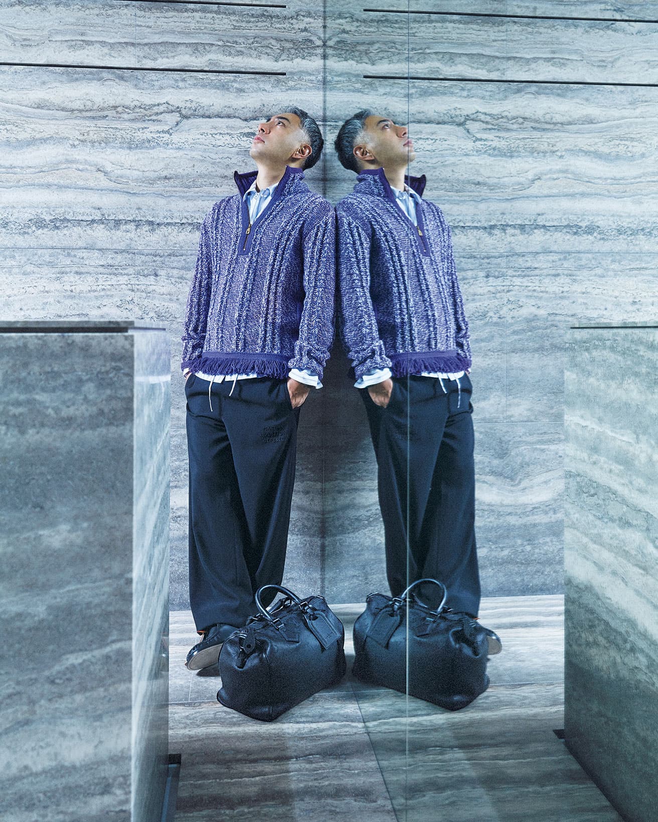 1階の床と壁や台座はすべてトラバーチンで統一。ジャカードニット426,800円、ストライプオーバーシャツ参考商品、ドローストリングパンツ196,900円、シューズ209,000円、バッグ1,507,000円（以上ルイ・ヴィトン／ルイ・ヴィトン クライアントサービス TEL 0120 00 1854）。