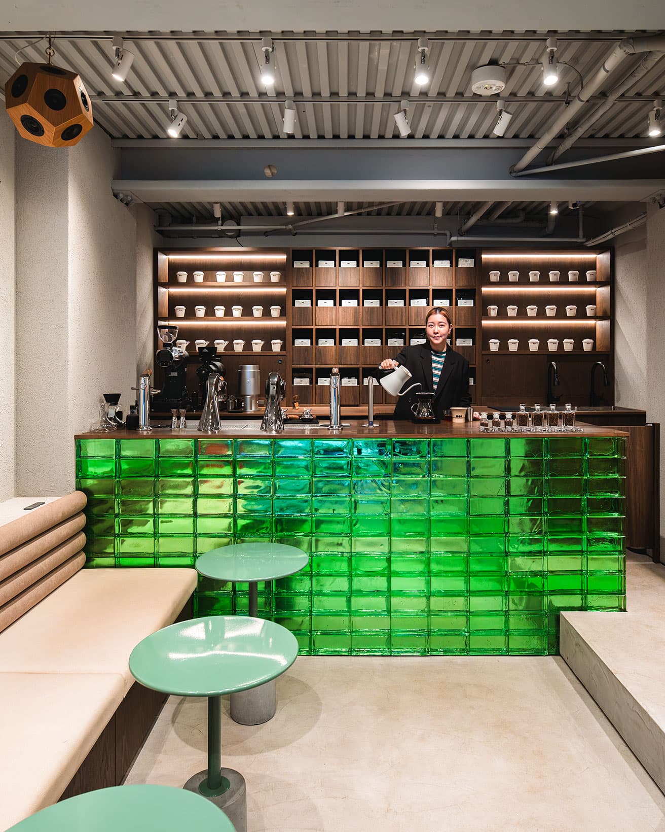 銀座店でハンドドリップするミランダさん。グリーンを基調にした店内は、ソファが連なり、丸テーブルが並ぶ。コーヒー豆は、漢方薬を収納する百味箪笥をイメージした棚に。